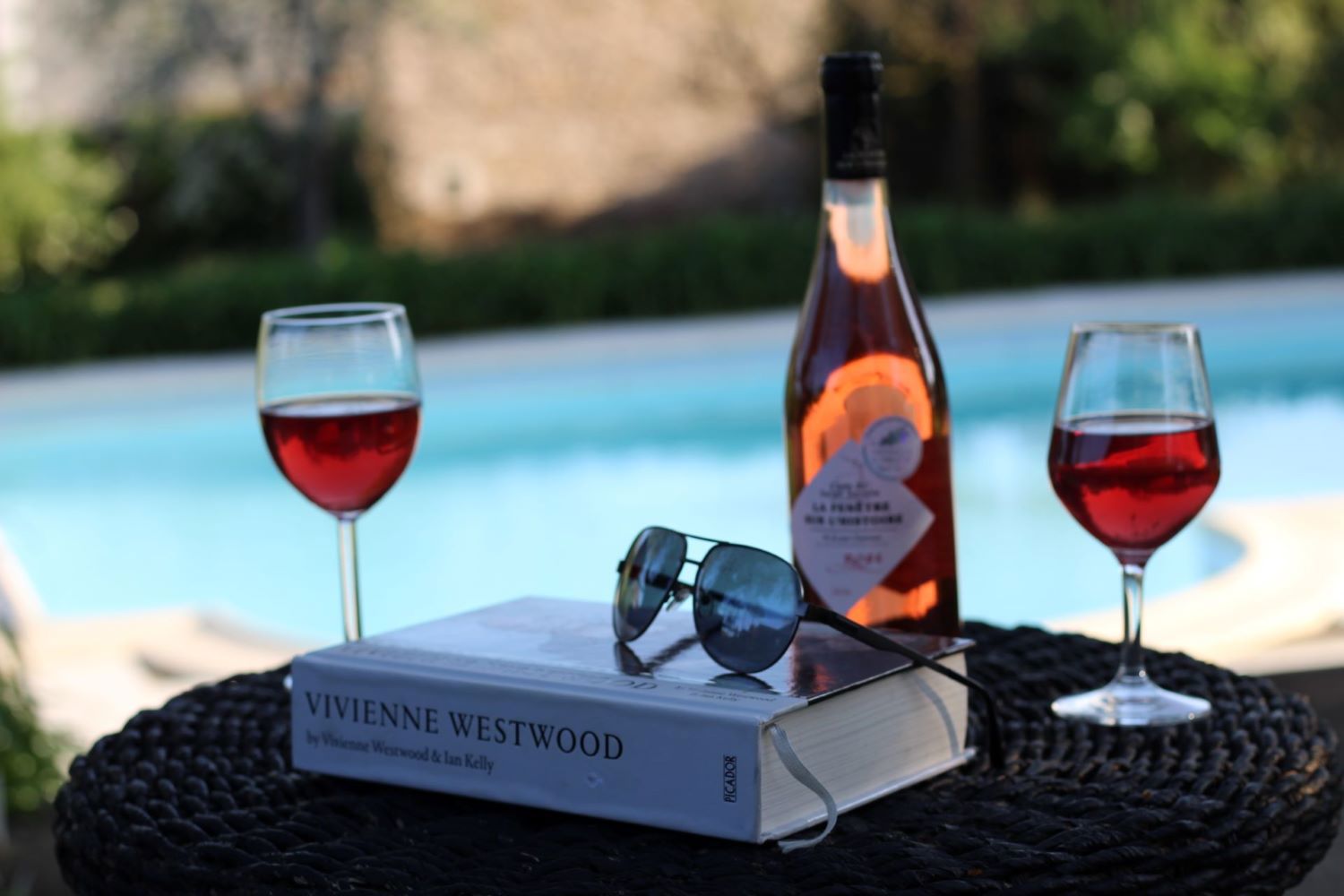 Reading book with wine A book and glasses of wine on a table near a pool, creating a serene and relaxing atmosphere.