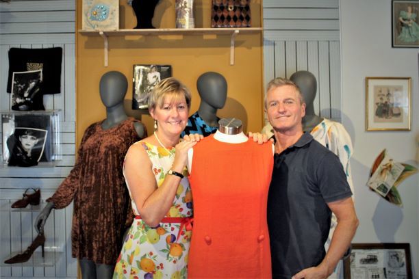 Man & woman with hands on shoulder of a healess mannequin wearing a 1960's orange sleeveless dress