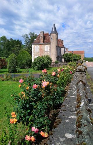 A road with a stone wall leading to a small beige chateau with a peppercorn silver turret,  amall 