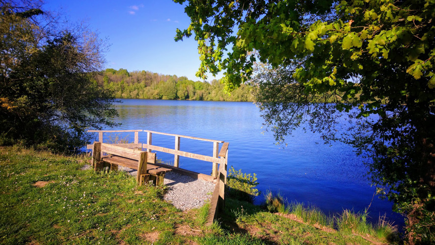 A wooden seat with wooden fence in front overlooking a very blue large lake 