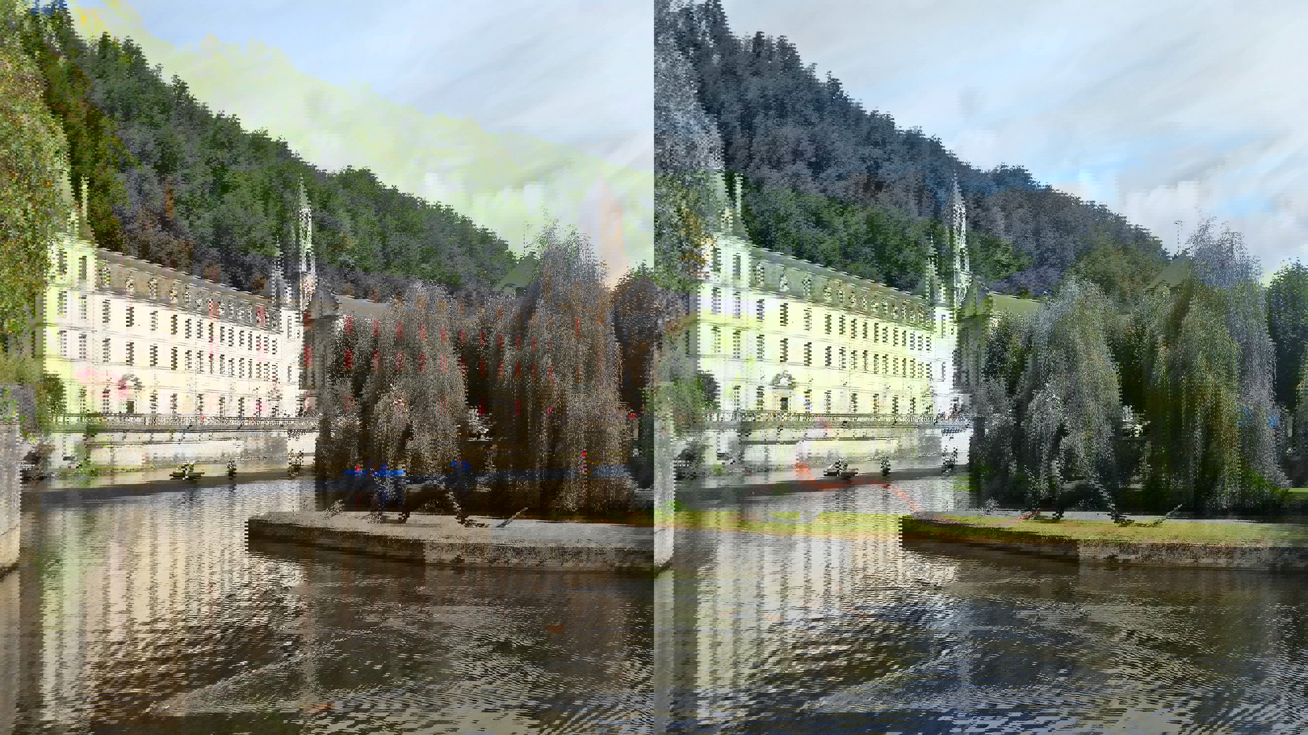 Brantome Venice of the North Perigord Long white 3 story building with pointed bell tower, located next to a river with trees
