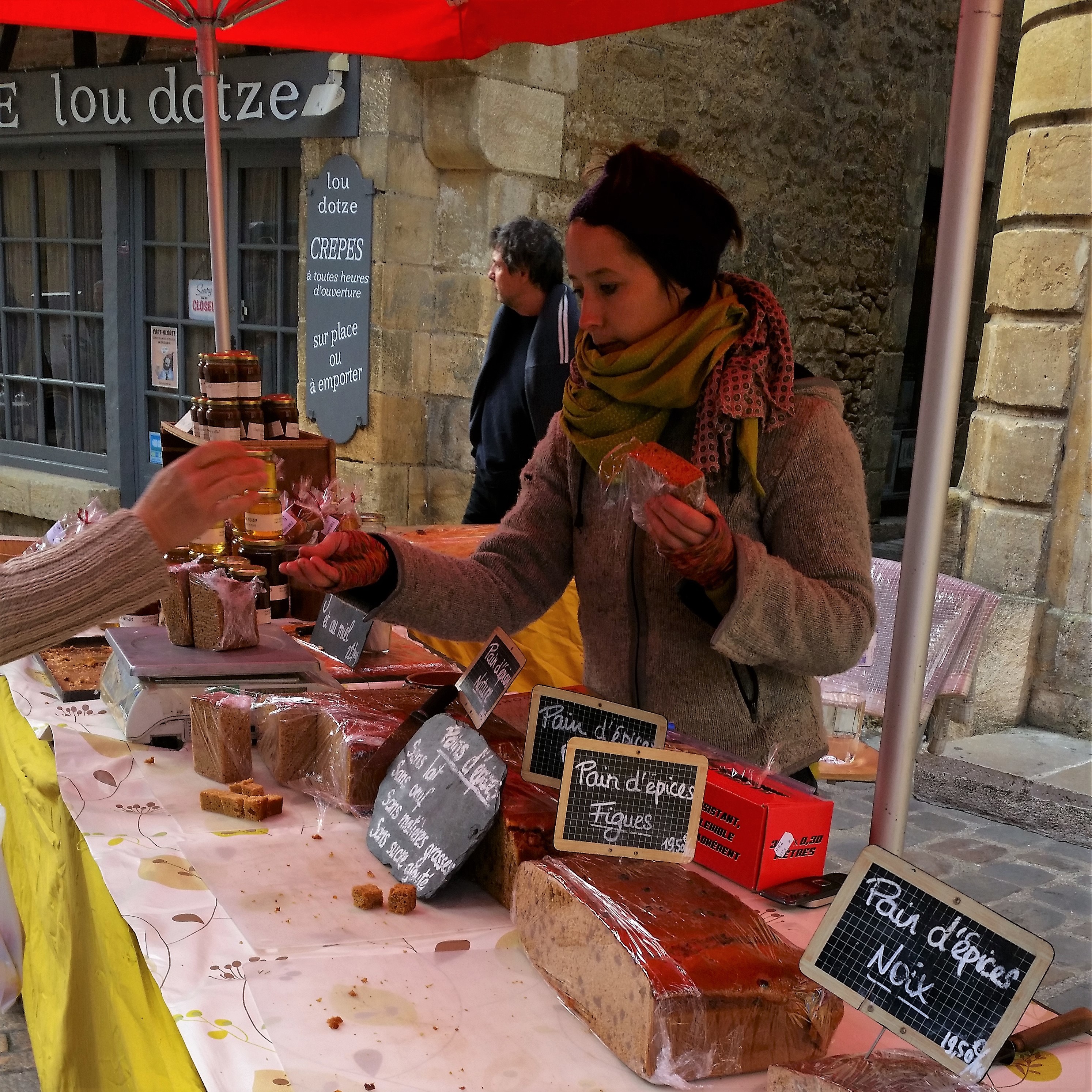 The Sunday market in Issigeac The Sunday market in Issigeac and woman wrapped up from cold selling gingerbread from a market stall