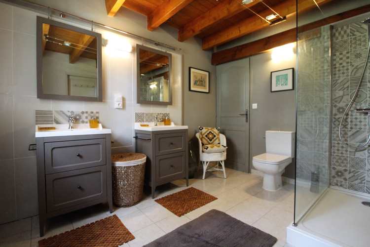 Beige bathroom with two sinks, a toilet and a walk in shower with grey patterned tiles 