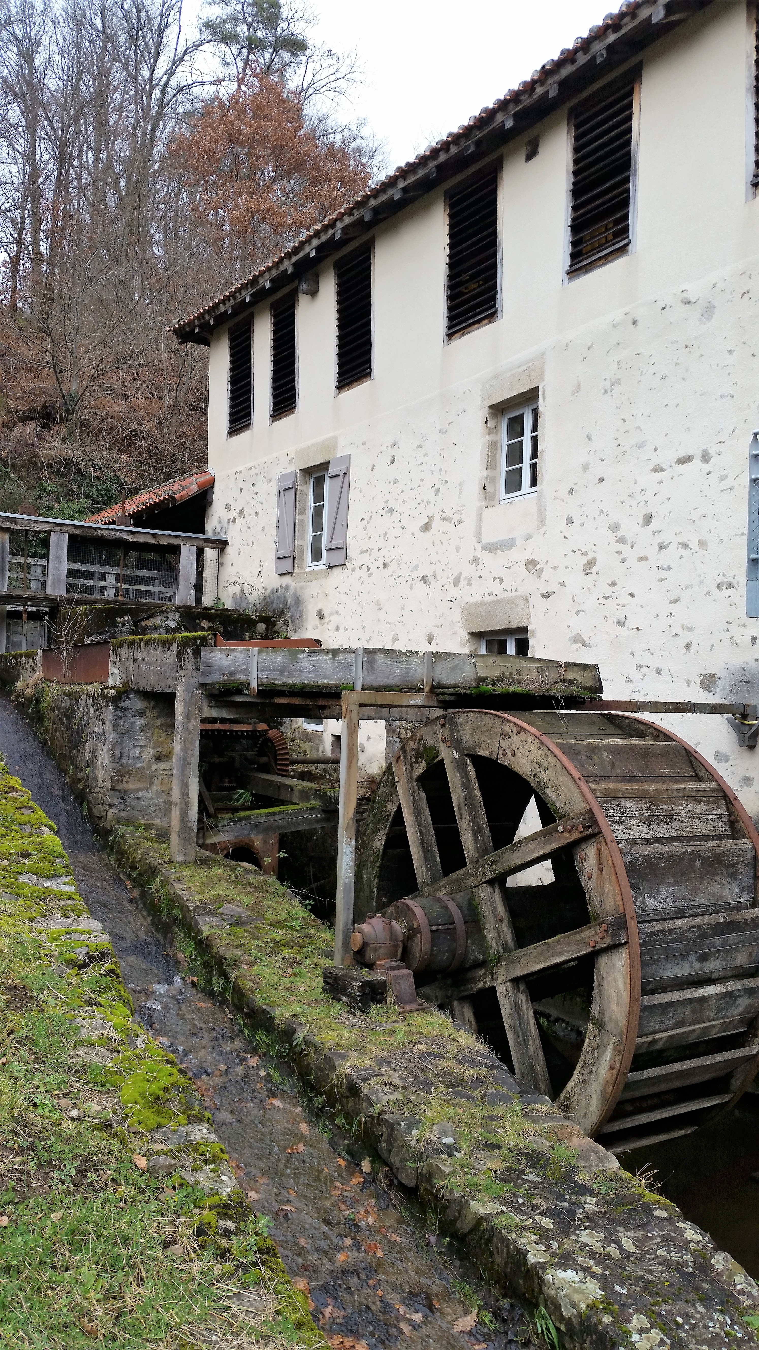Moulin de Got Old white 3 story building on slope with water wheel in wooded area