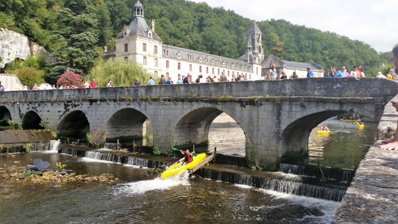 Canoeists paddling on the River Dronne beneath the medieval Pont Coudé bridge, Brantôme, Dordogne