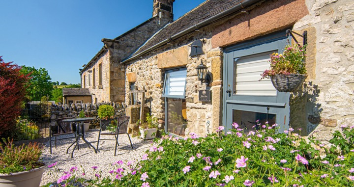 Close up of single storey stone barn with flowers in foreground